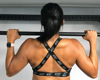 Rear view of a woman performing a pronated pull-up, hands shoulder-width on a pull-up bar showing engaged back muscles
